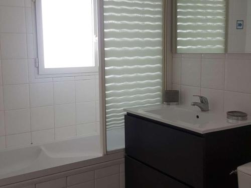 La salle de bains est pourvue d'un lavabo, d'une baignoire et d'une fenêtre. dans l'établissement Maison 90m² avec jardin, proche commerces et plages, équipée et idéale famille. - FR-1-494-120, à Vaux-sur-Mer