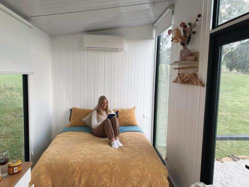 une femme assise sur un lit dans une chambre dans l'établissement Lotties Farm Tiny Homes, à One Tree Hill