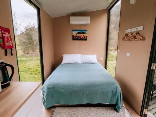 Bett in einem kleinen Zimmer mit einem großen Fenster in der Unterkunft Streamside Tiny House in Mangatarata