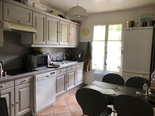 une cuisine avec des armoires blanches et une table et des chaises dans l'établissement Maison de ville avec jardin centre Montfort l'Amaury, à Montfort-lʼAmaury