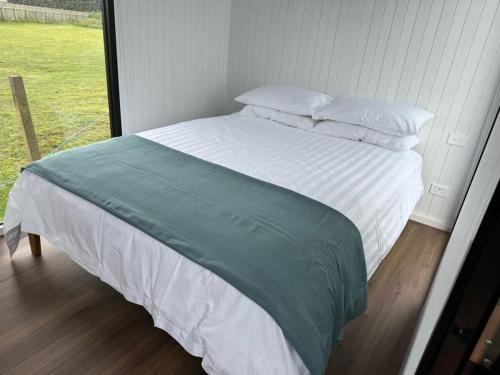 1 cama con sábanas y almohadas blancas y ventana en Rangiuru Stream Tiny home, en Otaki Beach
