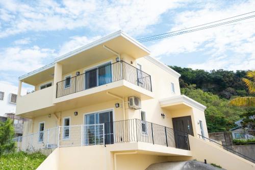 a white house with a balcony and trees at  M’sOceanⅡ Uruma in Uruma
