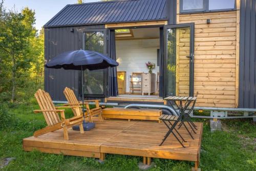 a tiny house with a deck with two chairs and an umbrella at Ammebergs Blommor by Tiny Away in Åmmeberg