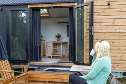 a woman sitting on a bench outside of a house at Ammebergs Blommor by Tiny Away in Åmmeberg