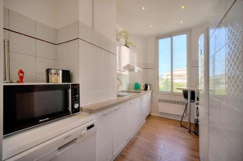 une cuisine avec des armoires blanches, un évier et un micro-ondes dans l'établissement Le Cal-3 Pièces-2 min Plage-VCA, à Cannes