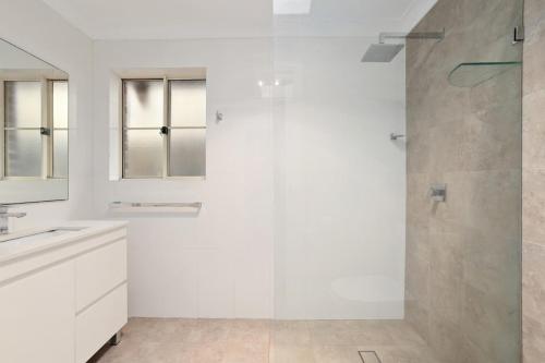 baño blanco con ducha y puerta de cristal en Hidden Hideaway - Family Friendly en Sídney
