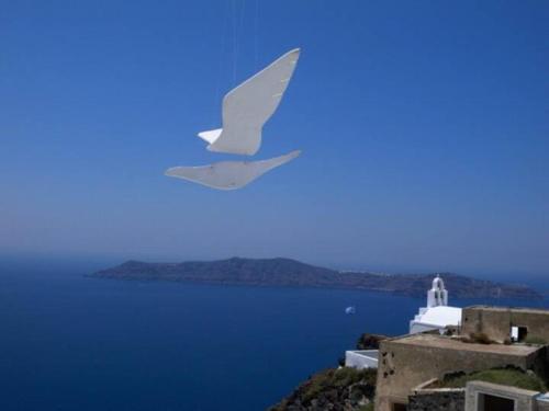 a white bird flying in the sky over the water at Altana Heritage Suites in Imerovigli