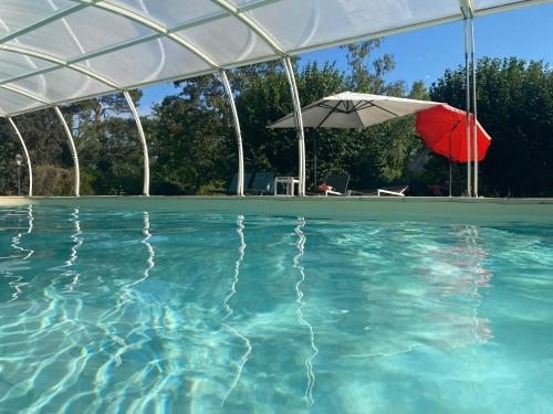 una piscina con una sombrilla roja y una blanca en Gîte du Gué Maraud, en Magny-Lormes