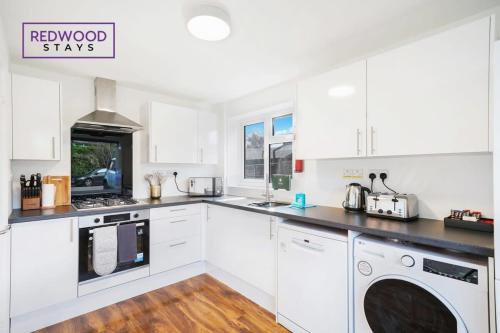 a kitchen with white cabinets and a washer and dryer at Cosy 3-Bedroom Serviced House with Free WiFi and Parking By Redwood Stays in Farnborough
