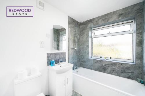 a bathroom with a white tub and a sink and a window at Cozy 3 Bed House with X2 FREE Parking By REDWOOD STAYS in Farnborough