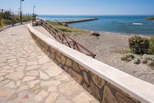 a stone wall next to a beach with the ocean at Beautiful bungalow on the Torrox-Costa boulevard! in Málaga