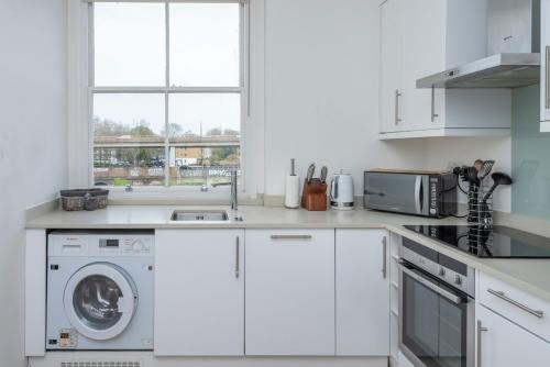 uma cozinha branca com uma máquina de lavar roupa e uma janela em BRAND NEW The Palms: Luxury Family Residence em Londres