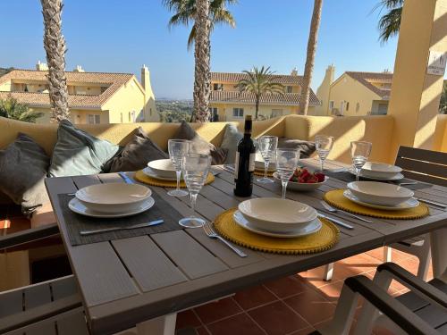 a wooden table with plates and wine glasses on a patio at La Manga Club Resort - 3 bedroom Duplex - La Colina in Atamaría