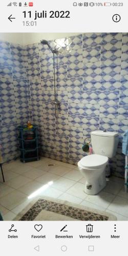 a bathroom with a toilet and a tiled wall at Chambre espacée et lumineuse in Mbour