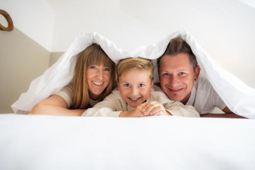 a family laying in bed under a blanket at SAUERLAND CHALETS - "Die Chalets Herzenssache" in Winterberg