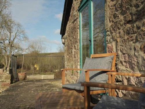 a wooden chair sitting next to a stone building at Noxon Pond Cottage in Clearwell