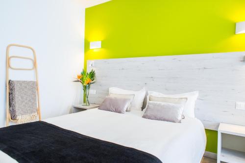 1 dormitorio con cama blanca y pared verde en Dunas Club - Hotel & Apartamentos, en Corralejo
