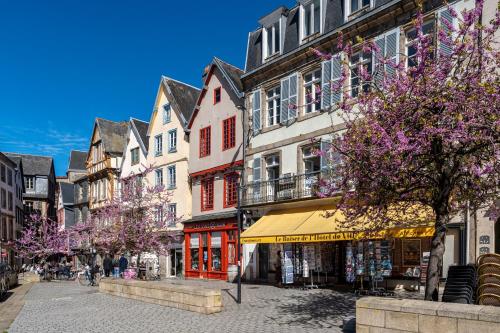 a city street with buildings and trees with purple flowers at Appartement du Théâtre Morlaix in Morlaix
