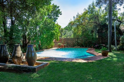 a swimming pool with two large vases in the grass at Waters on Willows in Pretoria