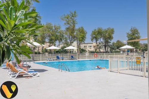 a pool at a resort with people sitting in chairs at Vogue Villa Near Golf/Ski Dubai/ Ibn Battuta Mall in Dubai