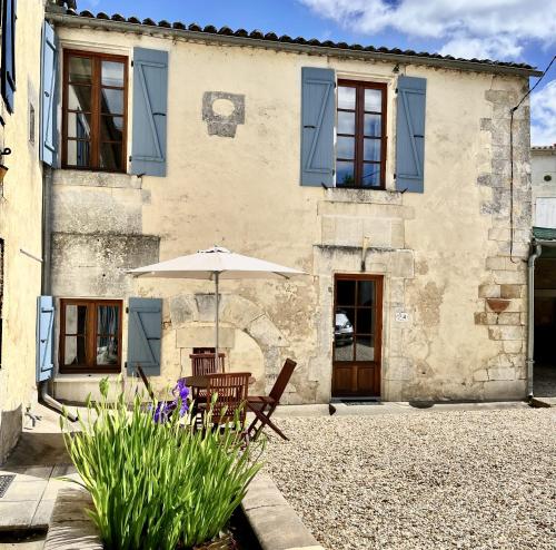 une maison avec un parasol et des chaises devant elle dans l'établissement Petit Moulin De Veillard, à Bourg-Charente