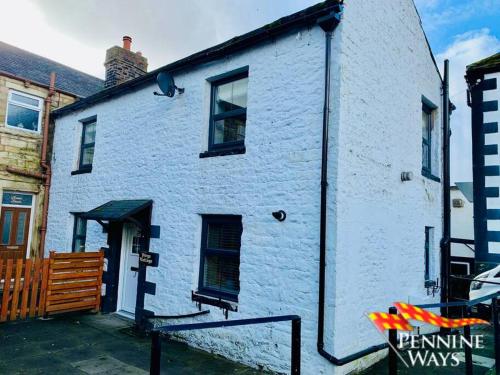 a white brick building with windows on a street at Forge Cottage - Centre of Britain in Haltwhistle