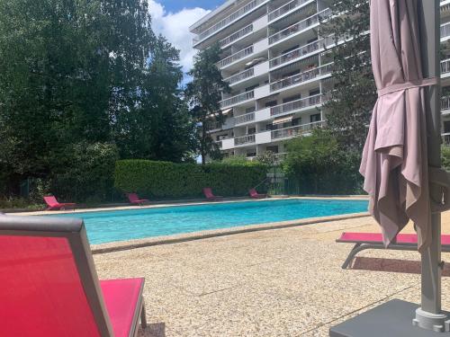 a swimming pool with chairs and an umbrella next to a building at Mont Royal - piscine - balcon vue imprenable sur les montagnes in Annecy