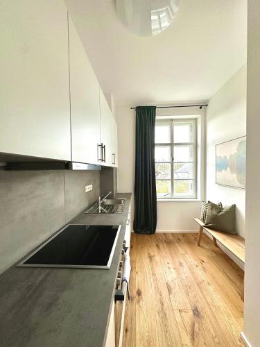 a kitchen with white cabinets and a wooden floor at betterplaces: Boutique Apartments - Frontenhausen in Dingolfing