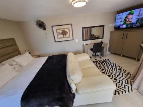 1 dormitorio con cama blanca, sofá y TV en Weston Guest House Krugersdorp, en Krugersdorp