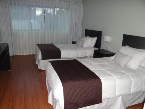 two beds in a hotel room with white and brown sheets at Hotel Del Rio in Constitución