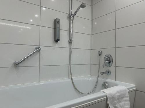 y baño de azulejos blancos con ducha y bañera. en PLAZA Hotel Föhr am Bodensee, en Friedrichshafen
