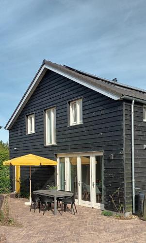 a black house with a picnic table and a yellow umbrella at Ons Huisje Achter in Noordwijkerhout