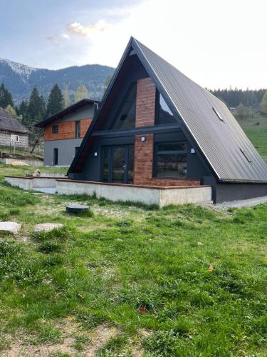 a house with a gambrel roof on a grass field at CabanA Oscar in Borşa