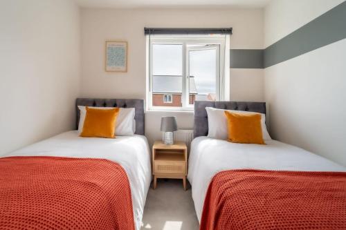 two beds with orange pillows in a room with a window at Huge Weekly & Monthly Savings - Free Parking - Wi-Fi & Netflix in Gloucester