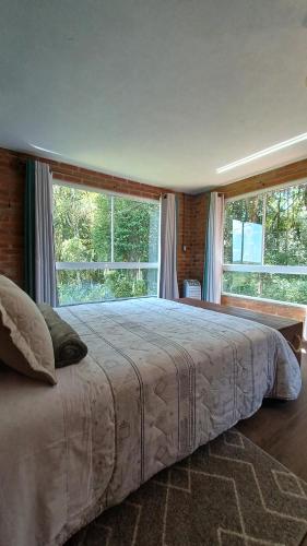 a bedroom with a large bed with two windows at Casa aconchegante em meio a natureza in Caxias do Sul