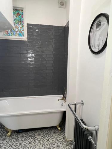 a bathroom with a white tub and a black tile wall at Sea Spray Victorian Apartment in St. Leonards