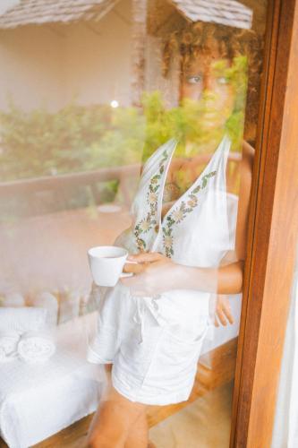 a woman is holding a cup in a window at CasaLô Hotel in Jericoacoara