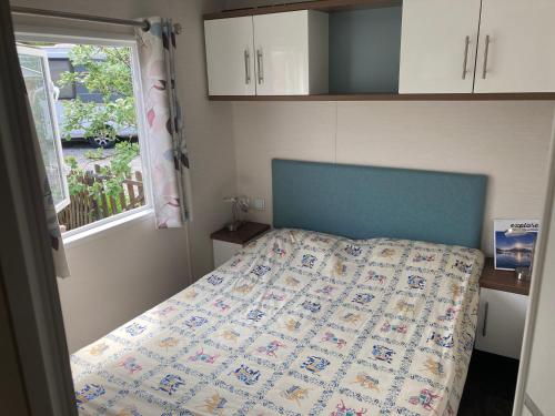 - une chambre avec un lit doté d'une tête de lit bleue et d'une fenêtre dans l'établissement mobilhome entre montagne et lac près de Gap au calme, à Rochebrune