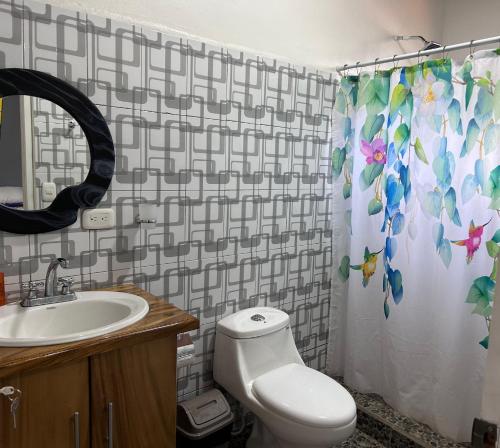 a bathroom with a toilet and a sink and a shower curtain at Hostal Mamá Derlys in Moyogalpa
