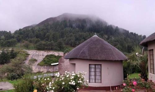 a small house with a thatched roof in front of a mountain at Letloepe Lodge in Qachaʼs Nek