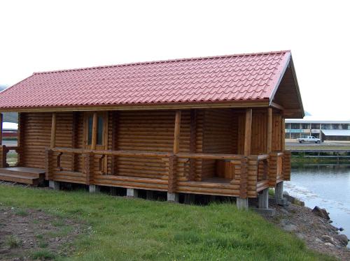 a wooden cabin with a red roof next to a body of water at Brimnes Bungalows in Ólafsfjörður
