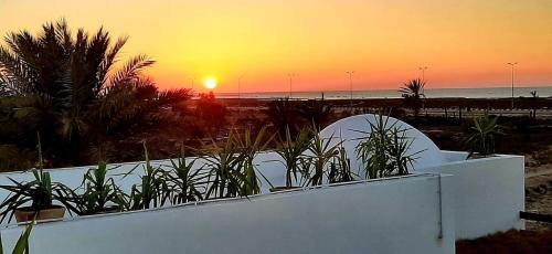 a sunset over the beach with a white fence and plants at Dar Cristina in Houmt Souk