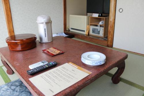 een tafel in een kamer met een koffiezetapparaat en afstandsbediening bij Kinokuniya Ryokan in Fujisawa