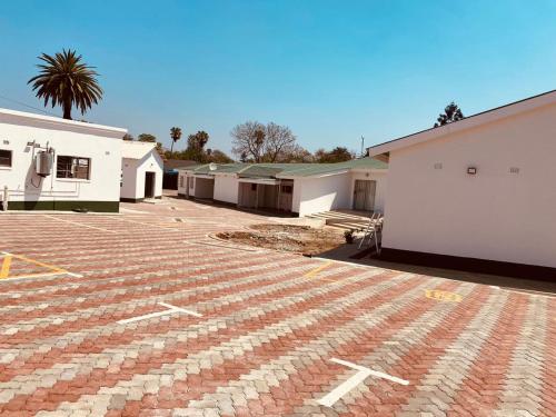 einen Backsteinparkplatz mit weißen Gebäuden und einer Palme in der Unterkunft Cumberland Guest Lodge in Bulawayo