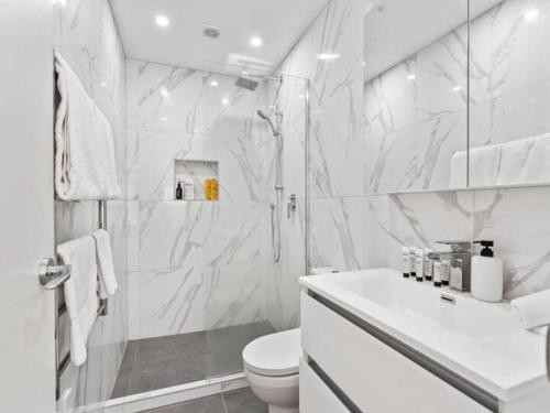uma casa de banho branca com um chuveiro e um WC. em Sleek Modern Pad next to Spark Arena Free Parking em Auckland