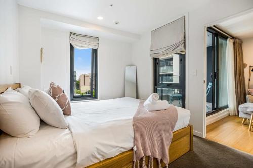 a white bedroom with a large bed and large windows at Cosy Two Bedroom Apartment with Balcony Pool and Gym in Auckland