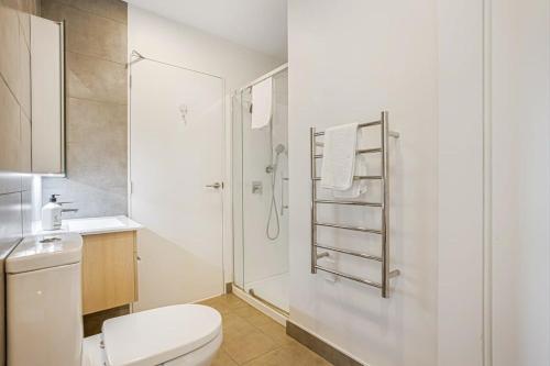 a white bathroom with a toilet and a shower at Cosy Two Bedroom Apartment with Balcony Pool and Gym in Auckland