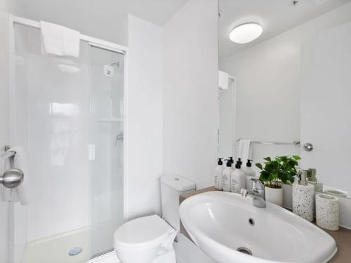 a white bathroom with a toilet and a sink at Central City 1BR Apartment in Auckland