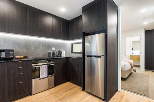 a kitchen with wooden cabinets and a stainless steel refrigerator at Sunny 1BR Retreat in Heart of CBD by Zodiak Stays in Auckland
