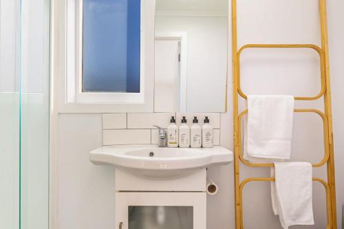 Baño blanco con lavabo y espejo en Stunning studio in Grey Lynn, en Auckland